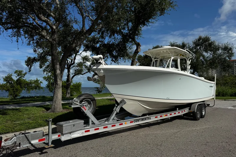 Slide: The Image of 2015 Sailfish 320 CC boat on trailer, parked near trees and water. - 6