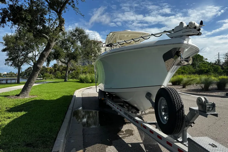 Slide: The Image of 2015 Sailfish 320 CC boat on trailer, parked near lush greenery and trees. - 8