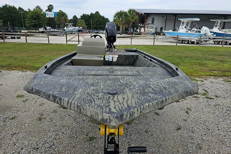 Slide: The Image of 2026 Tracker Grizzly 1648 SC boat with camouflage design, parked outdoors near a marina. - 4