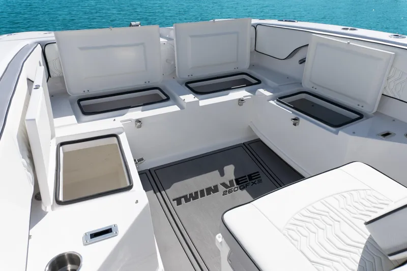 Slide: The Image of 2025 Twin Vee 260 GFX2 CC boat interior with open storage compartments, white seating, and ocean backdrop. - 29