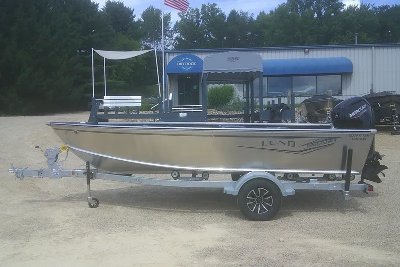 The Image of 2026 Lund 1800 Explorer Tiller boat on trailer, parked outdoors near a building. - 1