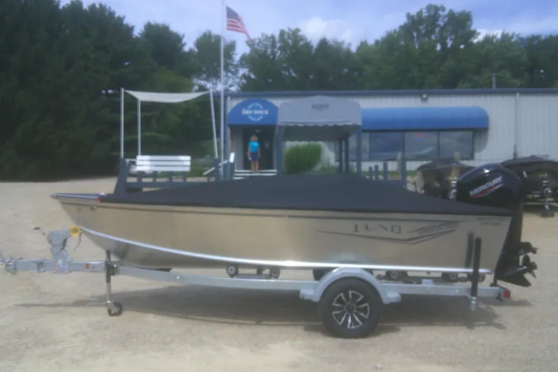 Slide: The Image of 2026 Lund 1800 Explorer Tiller boat on trailer, parked outdoors near a building. - 14