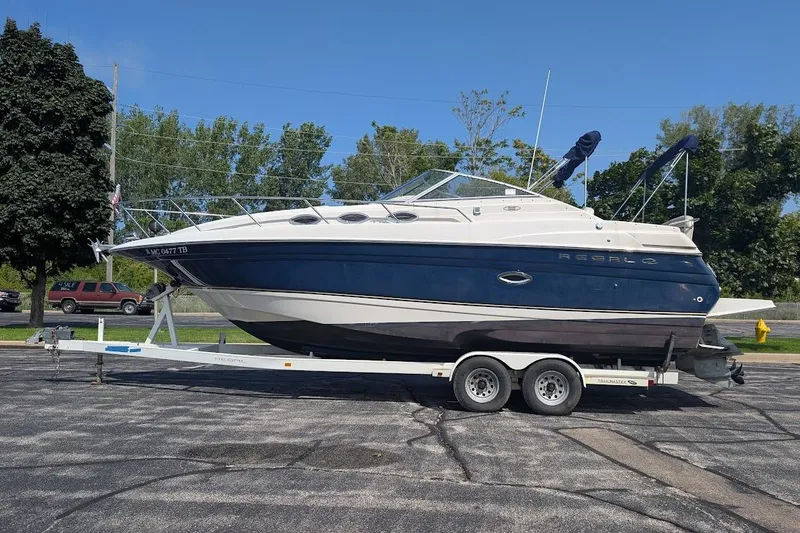 The Image of 2001 Regal Commodore 2660 boat on trailer, parked outdoors, surrounded by trees. - 1