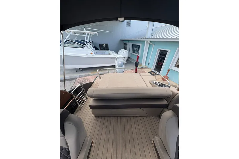 Slide: The Image of 2019 Bennington 25 QSBA boat interior with seating and cup holders, docked near a building. - 12