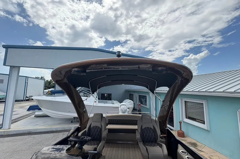 Slide: The Image of 2019 Bennington 25 QSBA boat with canopy, docked near blue building under cloudy sky. - 18