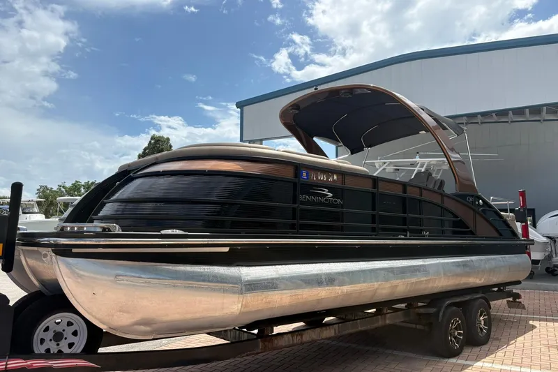 Slide: The Image of 2019 Bennington 25 QSBA pontoon boat on trailer, parked outdoors under a cloudy sky. - 24