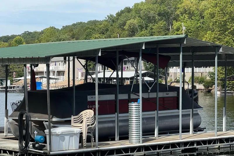 Slide: The Image of 2017 Crest II 250 SLE pontoon boat docked under a green-roofed shelter by the lake. - 1