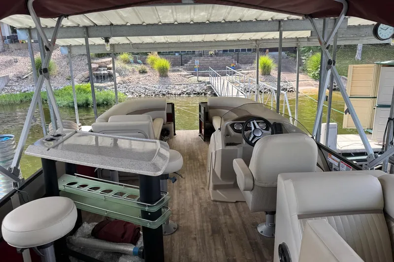 Slide: The Image of 2017 Crest II 250 SLE pontoon boat interior with seating and steering wheel, docked by a lakeside. - 11