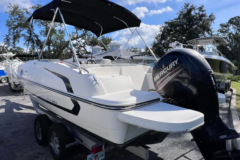 Slide: The Image of 2018 Bayliner 210 Deck Boat with Mercury outboard engine, parked on a trailer. - 3