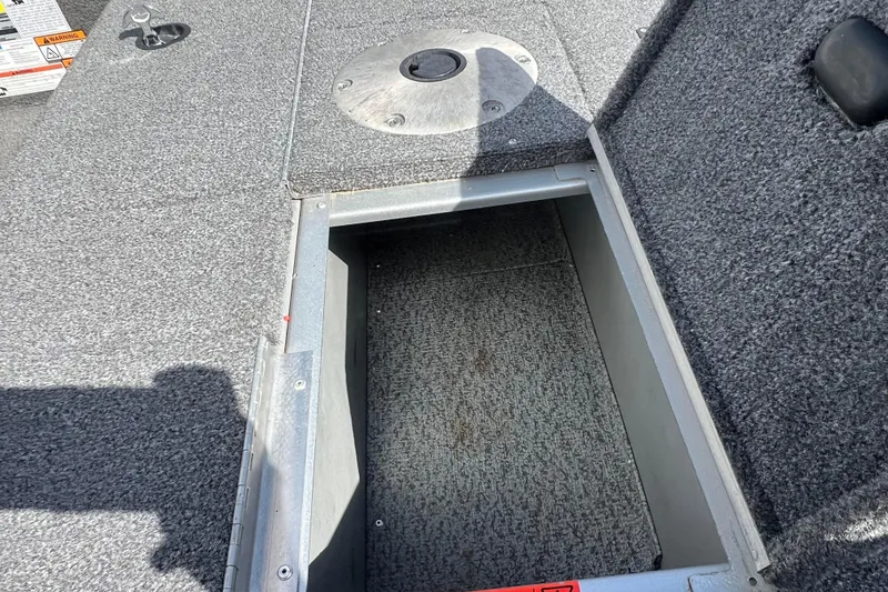 Slide: The Image of 2011 Alumacraft Classic 165 CS boat storage compartment with gray carpeted interior. - 19