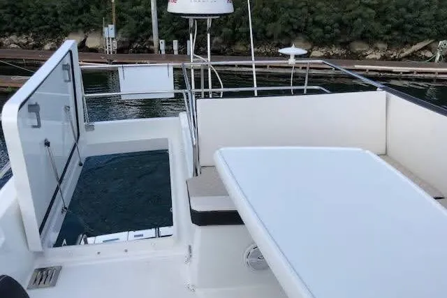 Slide: The Image of 2019 Jeanneau Velasco 37F yacht deck with seating and table, docked by lush greenery. - 38
