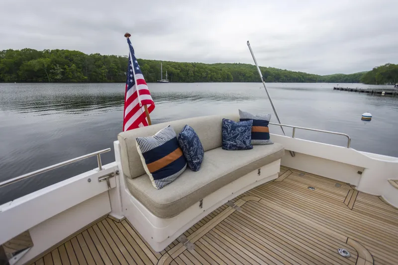 Slide: The Image of Grand Banks 46 Eastbay SX 2012 yacht deck with seating, cushions, and American flag by a serene lake. - 34