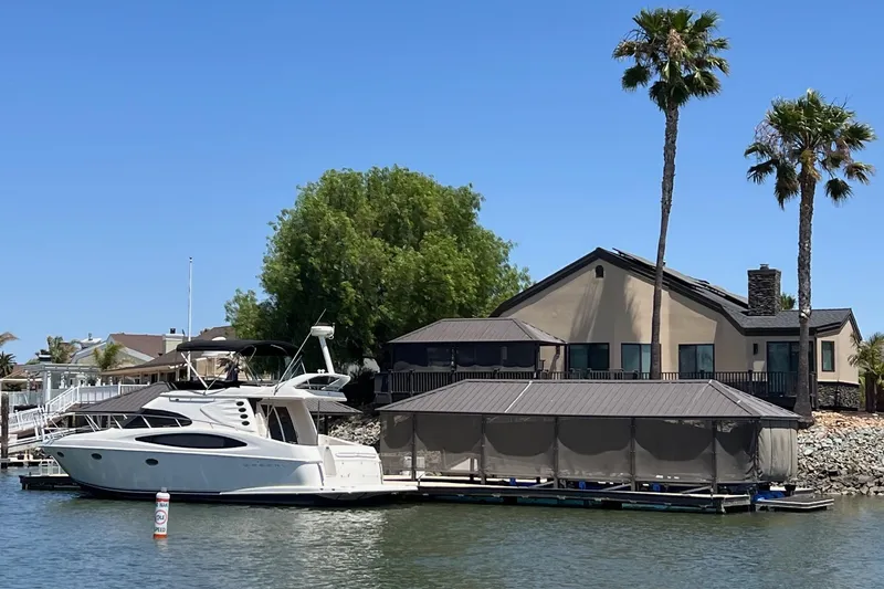 Slide: The Image of 2002 Regal Commodore 3880 yacht docked by a waterfront house with palm trees. - 3