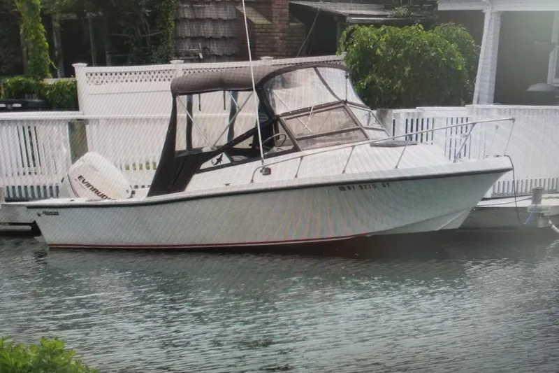 Slide: The Image of 1982 Mako 228 boat docked, featuring an Evinrude outboard motor and canopy. - 1