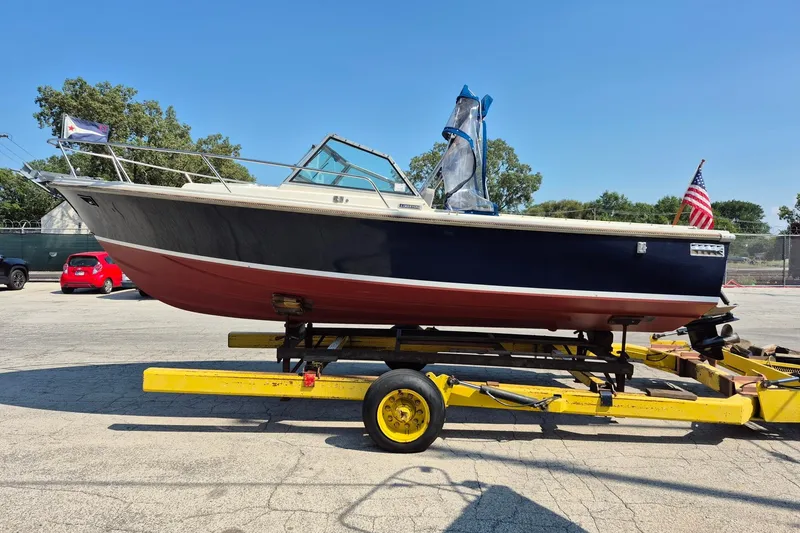 Slide: The Image of 1989 Limestone 24 boat on trailer, featuring a blue and red hull, parked outdoors. - 2