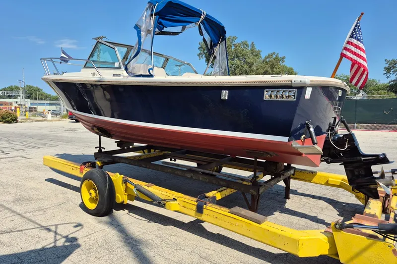 Slide: The Image of 1989 Limestone 24 boat on trailer with American flag, blue canopy, and red hull. - 3
