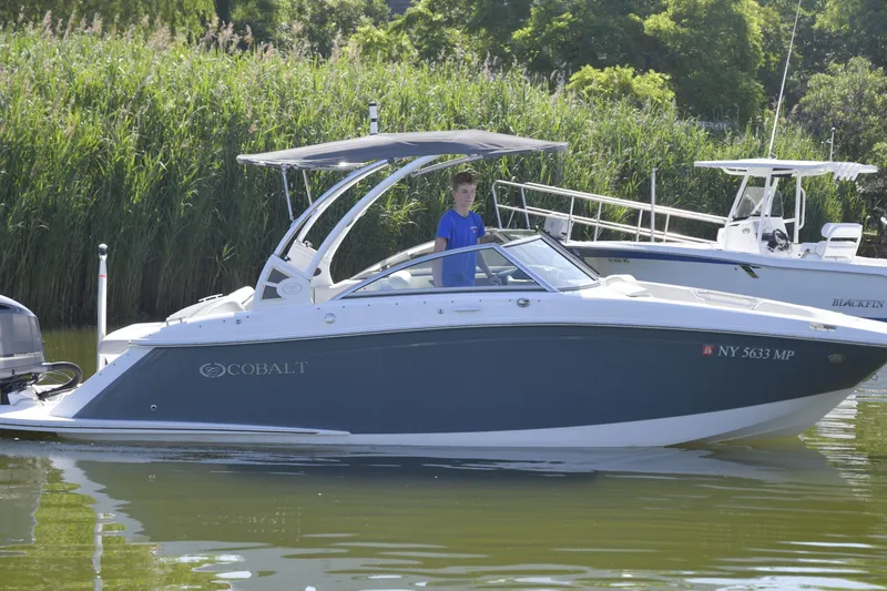 Slide: The Image of 2020 Cobalt 23SC boat on water, surrounded by lush greenery. - 2