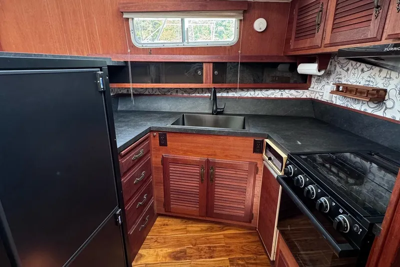 Slide: The Image of 1981 Tollycraft 43 Motor Yacht kitchen with wood cabinetry, black countertops, and modern appliances. - 16