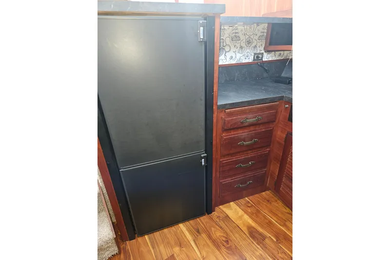 Slide: The Image of 1981 Tollycraft 43 Motor Yacht kitchen with black fridge, wooden cabinets, and patterned backsplash. - 19