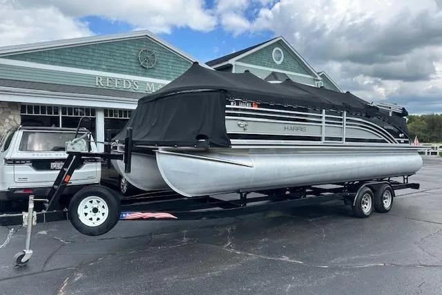 Slide: The Image of 2020 Harris Solstice 250 pontoon boat on trailer, parked outside a building under cloudy skies. - 38