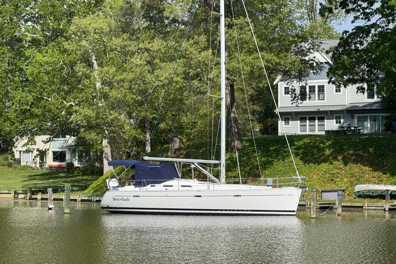 Slide: The Image of Beneteau Oceanis 393 sailboat docked by a lakeside house, surrounded by lush greenery. - 25