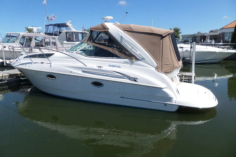 Slide: The Image of 2003 Doral 280 SE boat docked in marina, featuring sleek design and beige canopy. - 2