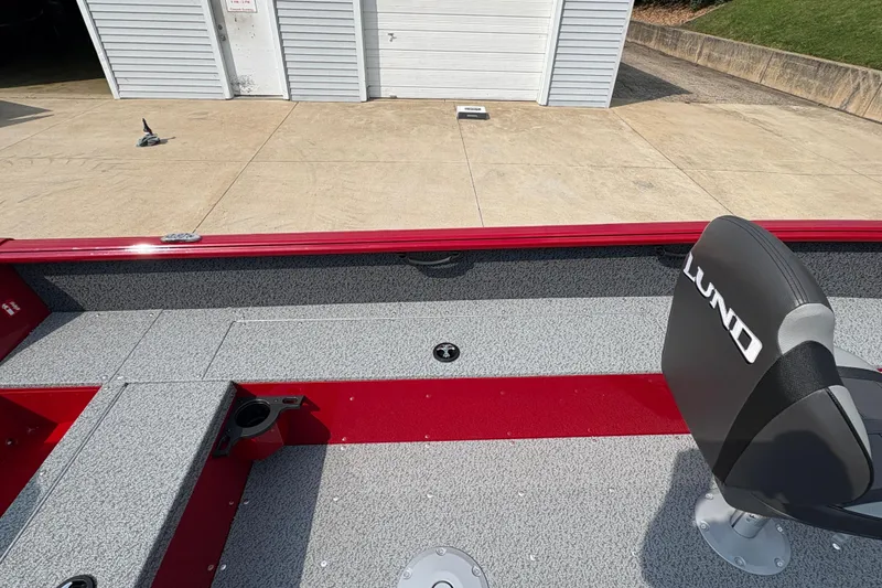Slide: The Image of 2026 Lund 1800 Explorer SS boat interior with gray and red seating, docked near a garage. - 23