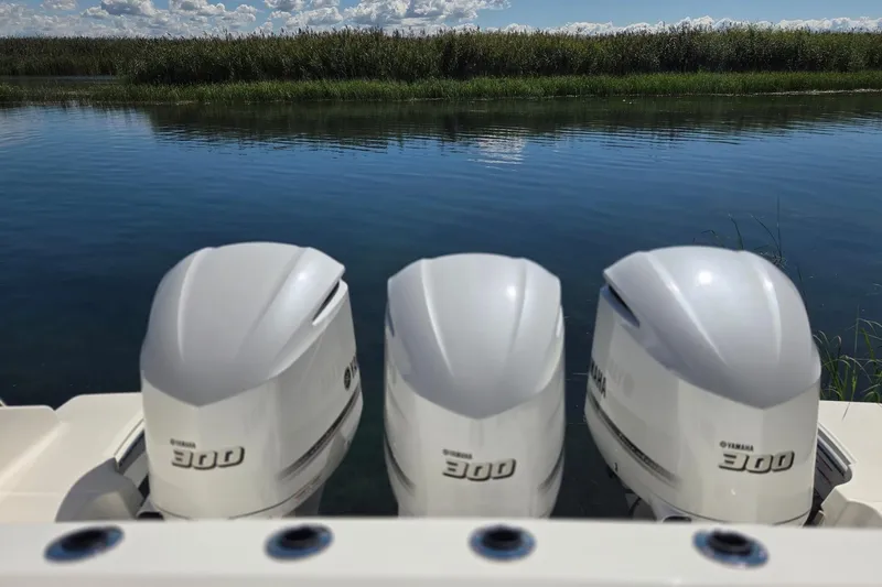 Slide: The Image of Triple Yamaha 300 engines on a 2020 Pursuit DC 365 Dual Console boat by a serene lake. - 19