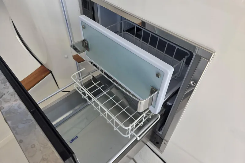 Slide: The Image of 2020 Pursuit DC 365 Dual Console boat storage compartment with wire basket and cutting board. - 37