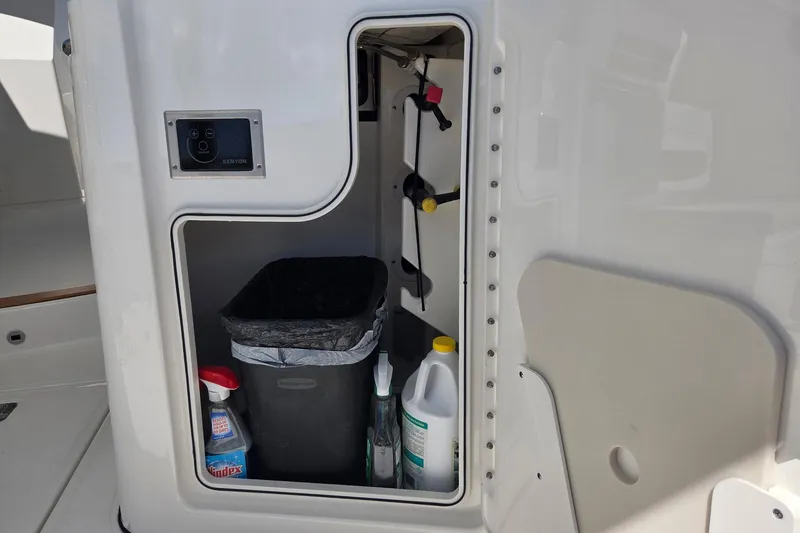 Slide: The Image of Storage compartment on a 2020 Pursuit DC 365 Dual Console boat with cleaning supplies. - 42