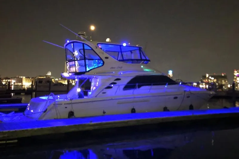The Image of 2002 Sea Ray 550 Sedan Bridge yacht illuminated with blue lights at night in a marina. - 0