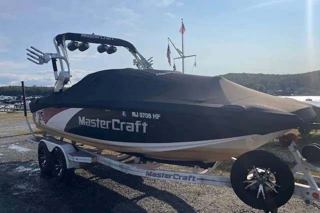 Slide: The Image of 2013 MasterCraft X-25 boat on trailer, covered, parked near a lake with flags in the background. - 20