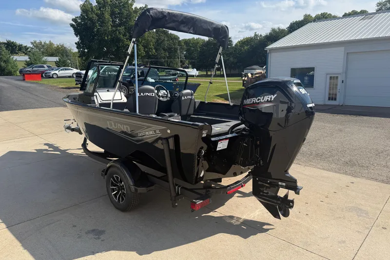 Slide: The Image of 2026 Lund 1650 Rebel XL Sport boat with Mercury 90 engine, parked outdoors. - 4