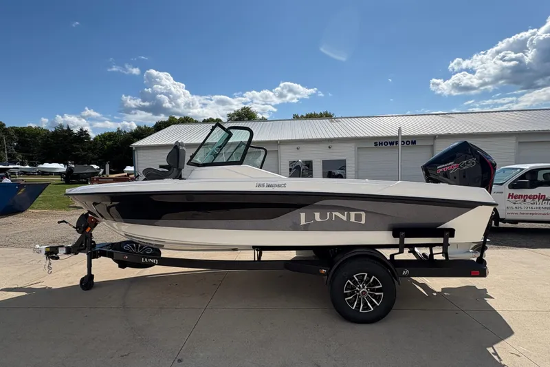Slide: The Image of 2026 Lund 185 Impact GL boat on trailer, parked outside showroom under blue sky. - 4