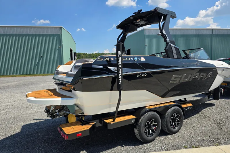 Slide: The Image of 2026 Supra SA boat on trailer, black and white design, parked near green building. - 6
