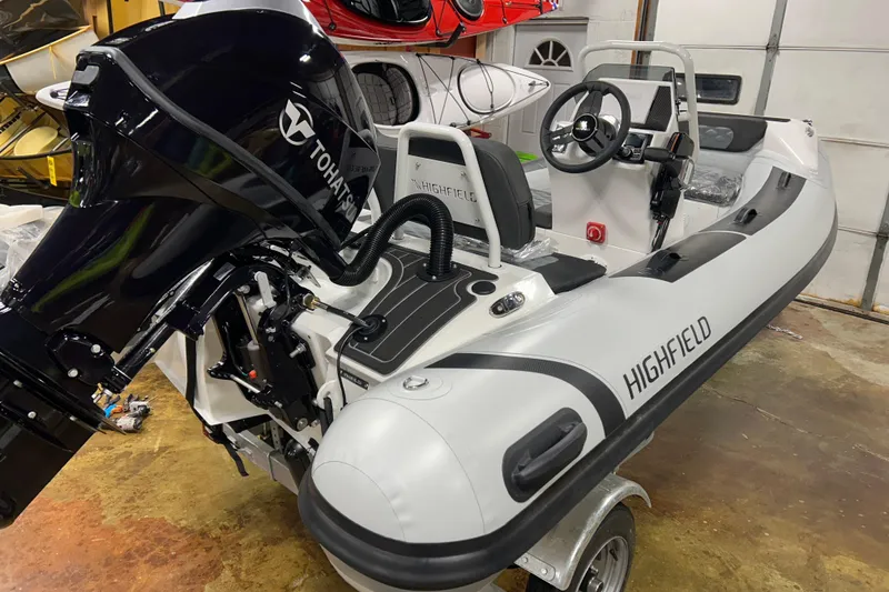 Slide: The Image of 2026 Highfield Sport 360 inflatable boat with Tohatsu outboard motor in a garage setting. - 4