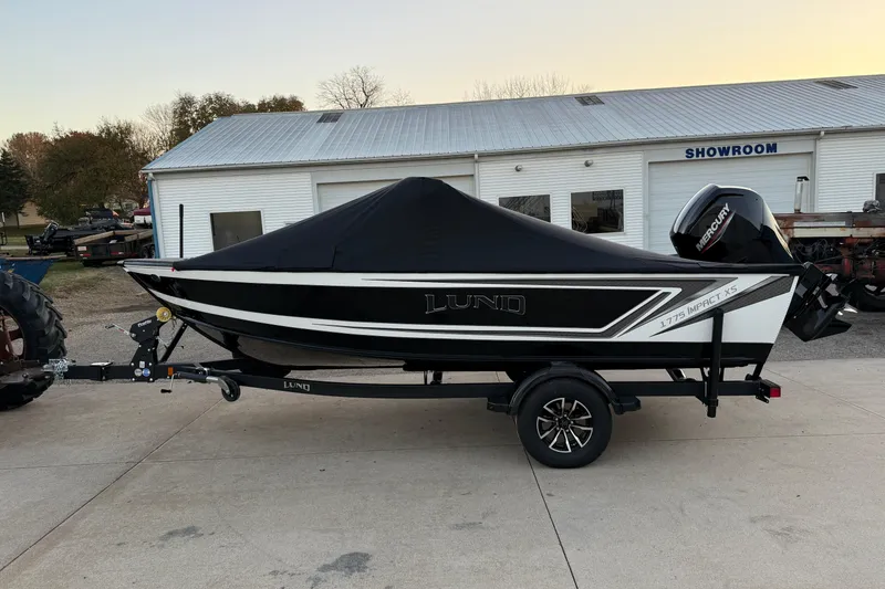 Slide: The Image of 2026 Lund 1775 Impact XS Sport boat with cover, parked outside a showroom. - 26