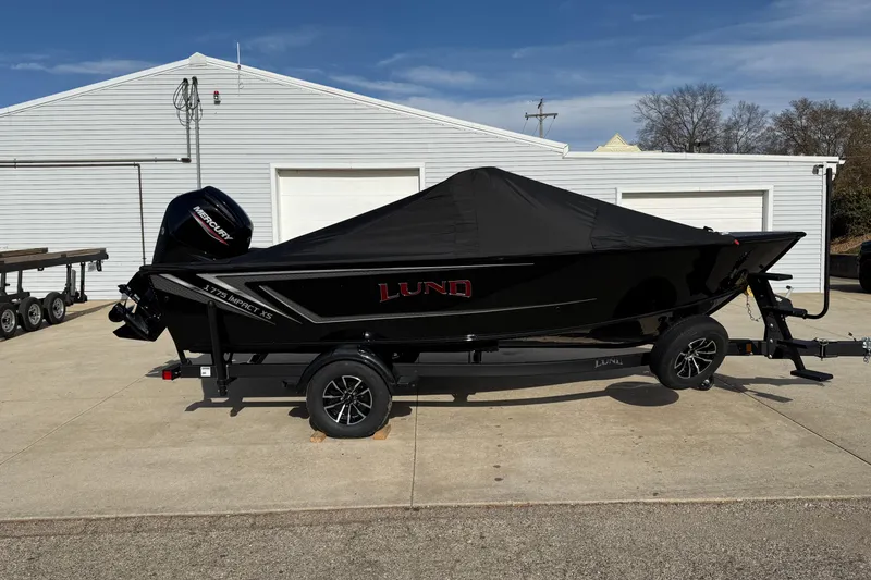 Slide: The Image of 2026 Lund 1775 Impact XS Sport boat with cover on trailer, parked outside a garage. - 30