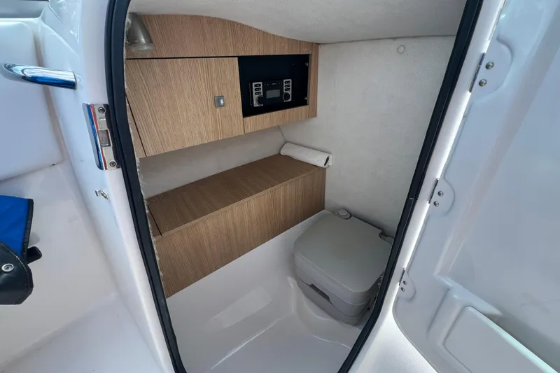 Slide: The Image of 2015 Robalo R227 Dual Console boat interior with compact toilet and wooden cabinetry. - 17