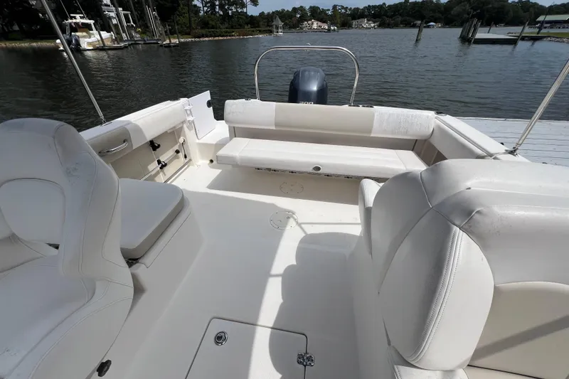Slide: The Image of 2015 Robalo R227 Dual Console boat interior with white seating, docked by a calm lake. - 36
