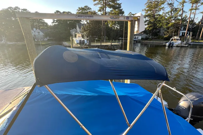 Slide: The Image of 2015 Robalo R227 Dual Console boat with blue canopy on a serene waterfront. - 66