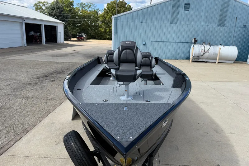 Slide: The Image of 2026 Lund 1800 Explorer Tiller boat with dual seats, parked near industrial buildings. - 2