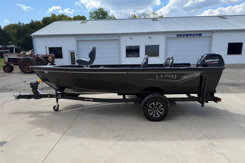 Slide: The Image of 2026 Lund 1800 Explorer Tiller boat on trailer outside showroom, featuring Mercury engine. - 4