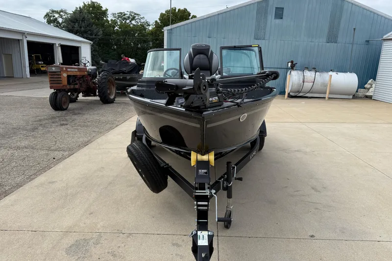 Slide: The Image of 2026 Lund 1800 Explorer Sport boat on trailer, parked near farm equipment and buildings. - 2