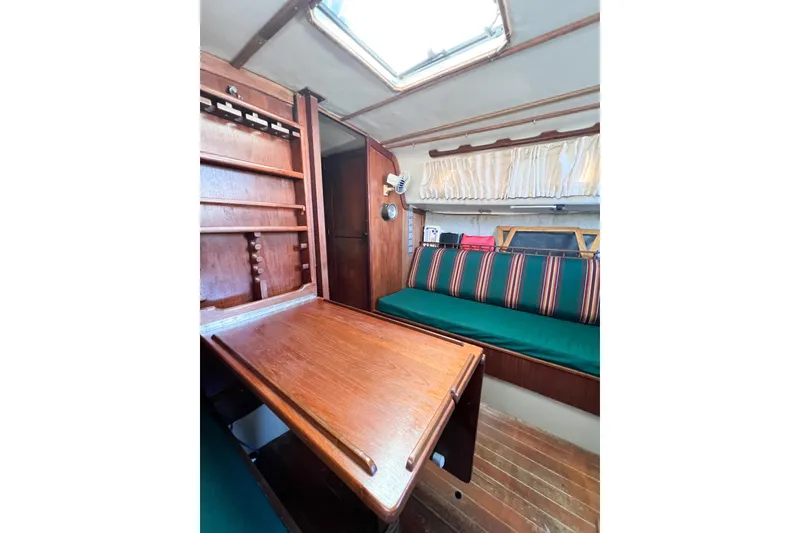 Slide: The Image of 1978 CAL 34 sailboat interior with wooden table, striped seating, and storage shelves. - 23