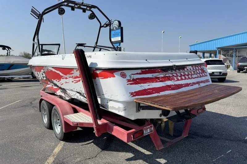 Slide: The Image of 2000 Tigé 2300V Limited boat on trailer with American flag design, parked outdoors. - 6