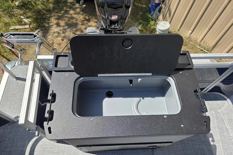 Slide: The Image of 2026 Sun Tracker SF 20 DLX boat with open storage compartment, outdoor setting. - 18