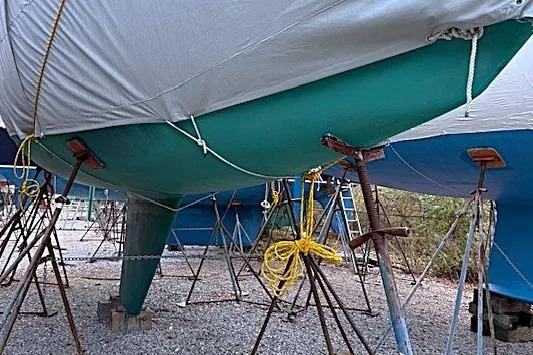 Slide: The Image of 1985 Sabre 36 sailboat on stands, covered and secured, in a boatyard setting. - 23