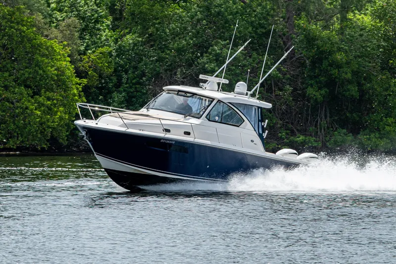 The Image of Pursuit boat cruising on water with lush green trees in the background. - 0