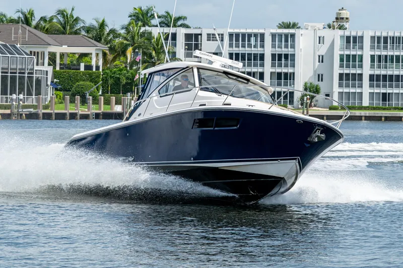Slide: The Image of Pursuit boat cruising on water near modern waterfront buildings and palm trees. - 2